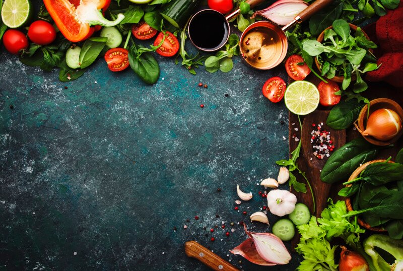 Fresh healthy food cooking or salad making ingredients on dark background with rustic wooden board. Diet or vegetarian food concept. Top view, copy space